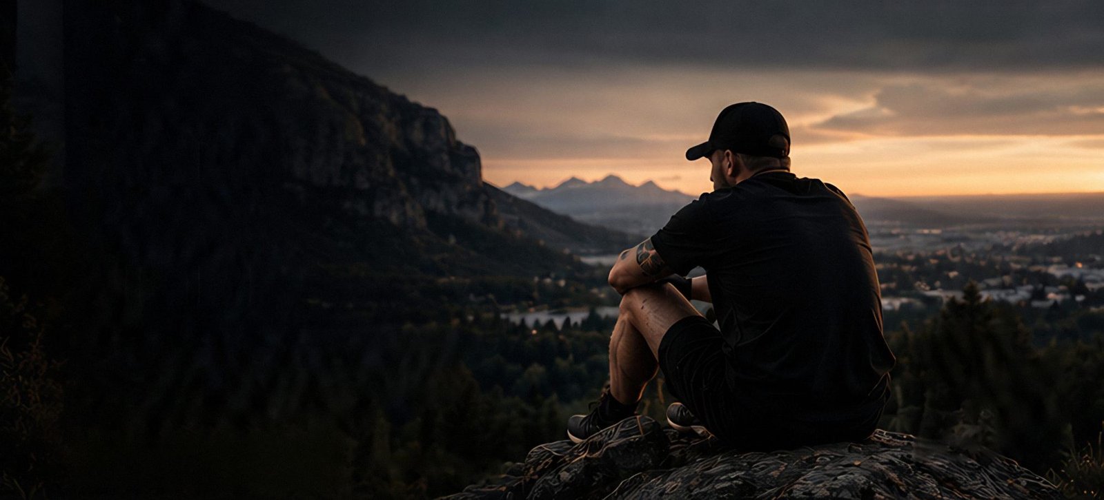 Man sitting on a rocky outcrop at sunset, looking out over a valley